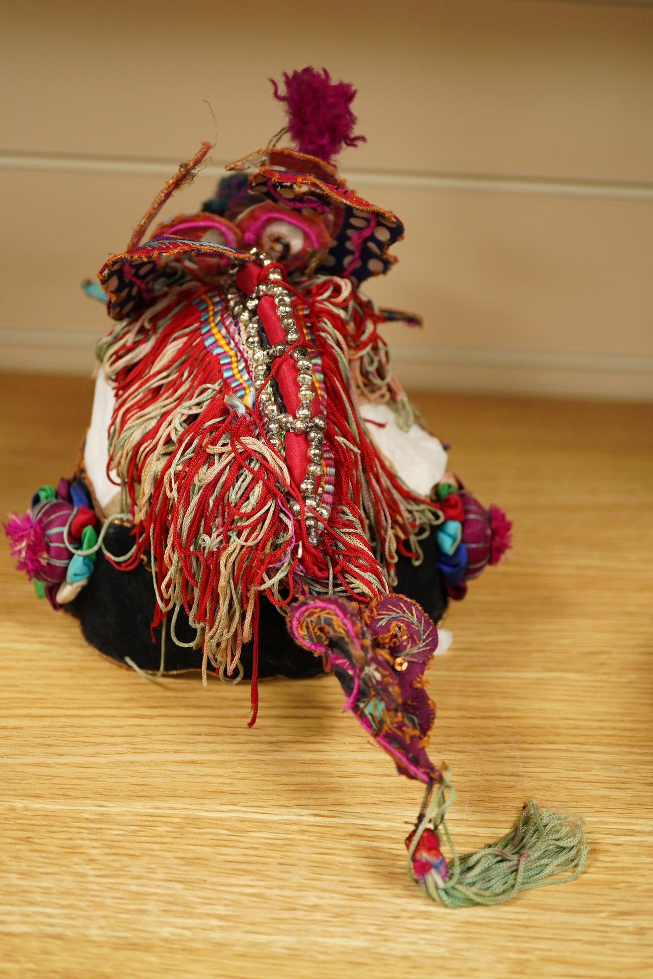 A decorative Chinese child’s festival ‘dragon’ hat, decorated with embroidered panels, tasselling and pom-poms with an elaborate dragon face and head dress. 20cm high. Condition - tasselling is missing around the dragons